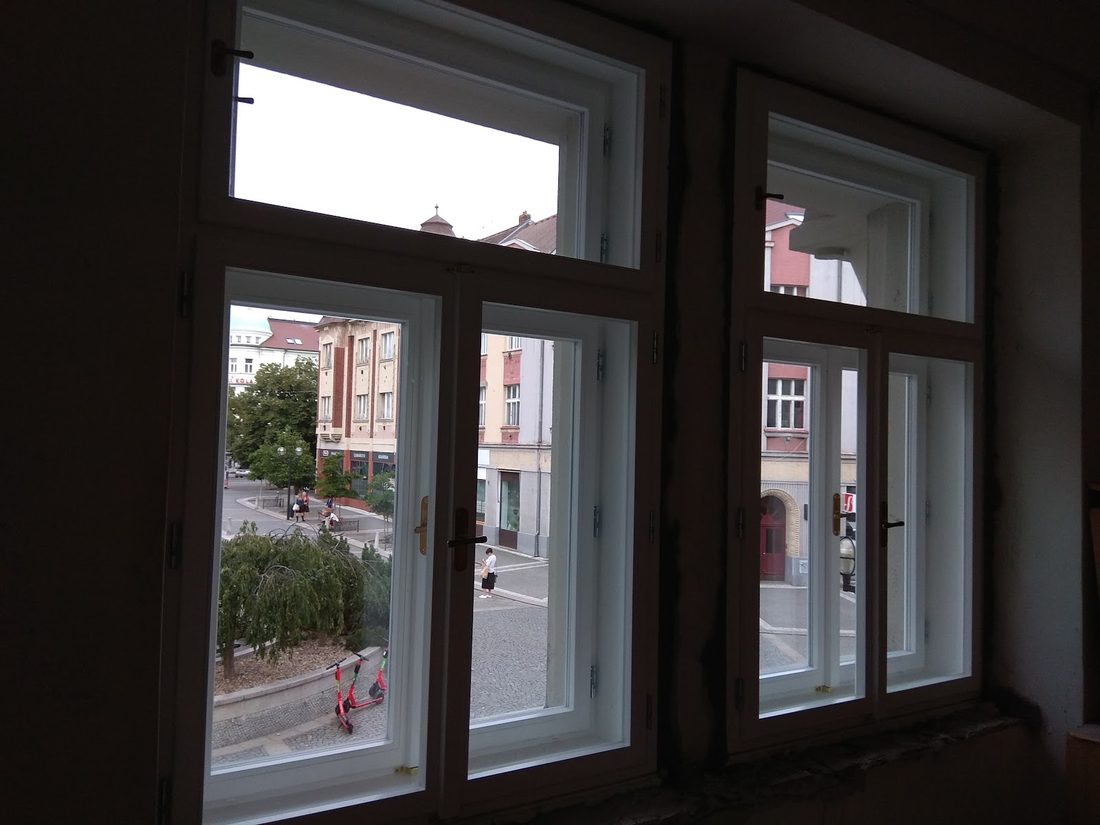 Nová bílá dřevěná okna v místnosti, za nimi ulice